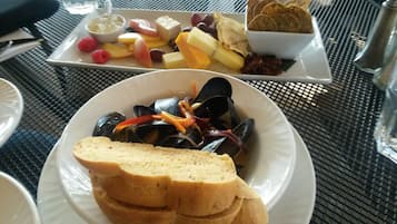 Ein Esstisch mit einer Platte Miesmuscheln, Brot und einer Schüssel mit Obst und Käse.