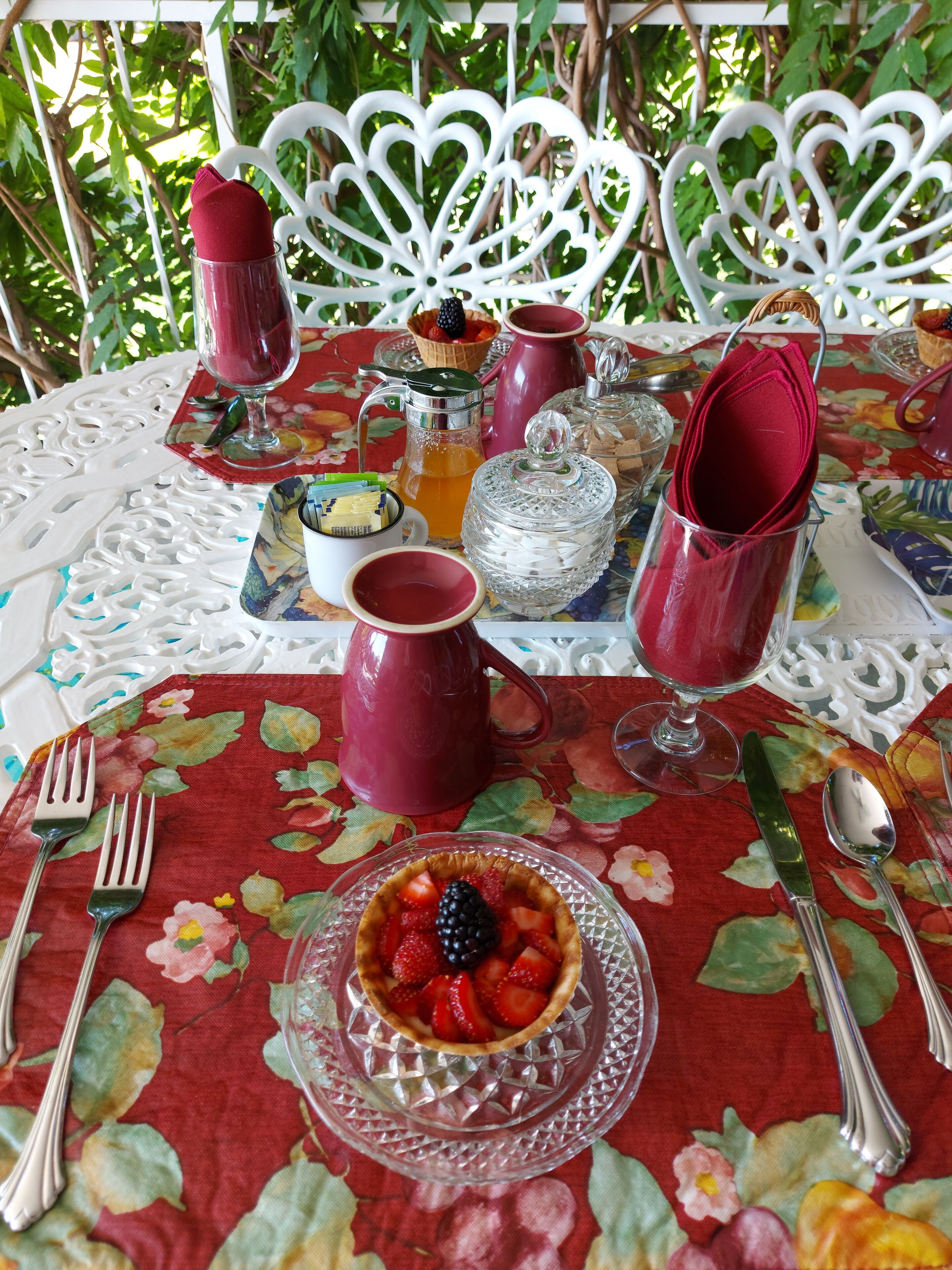 Ein gedeckter Tisch mit blumigem Tischläufer, einer Kuchenform mit Obst und verschiedenen Geschirrteilen.