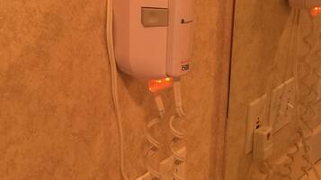 A hair dryer mounted on a wall with a cord, a power outlet, and a switch.