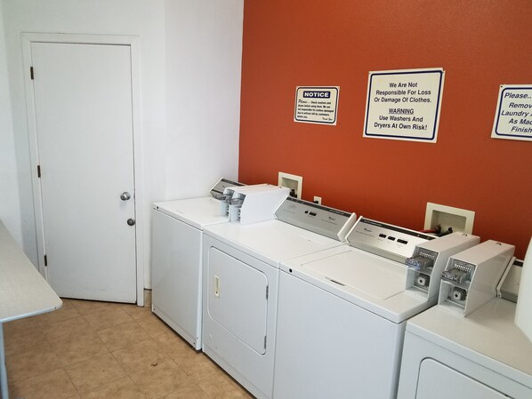 A laundry room with three washers and dryers, a white door, and three warning signs on the wall. - Gridley Inn & RV Park (Gridley)