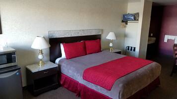 Una habitación de hotel con una cama, dos mesitas de noche con lámparas, un microondas y un refrigerador pequeño.