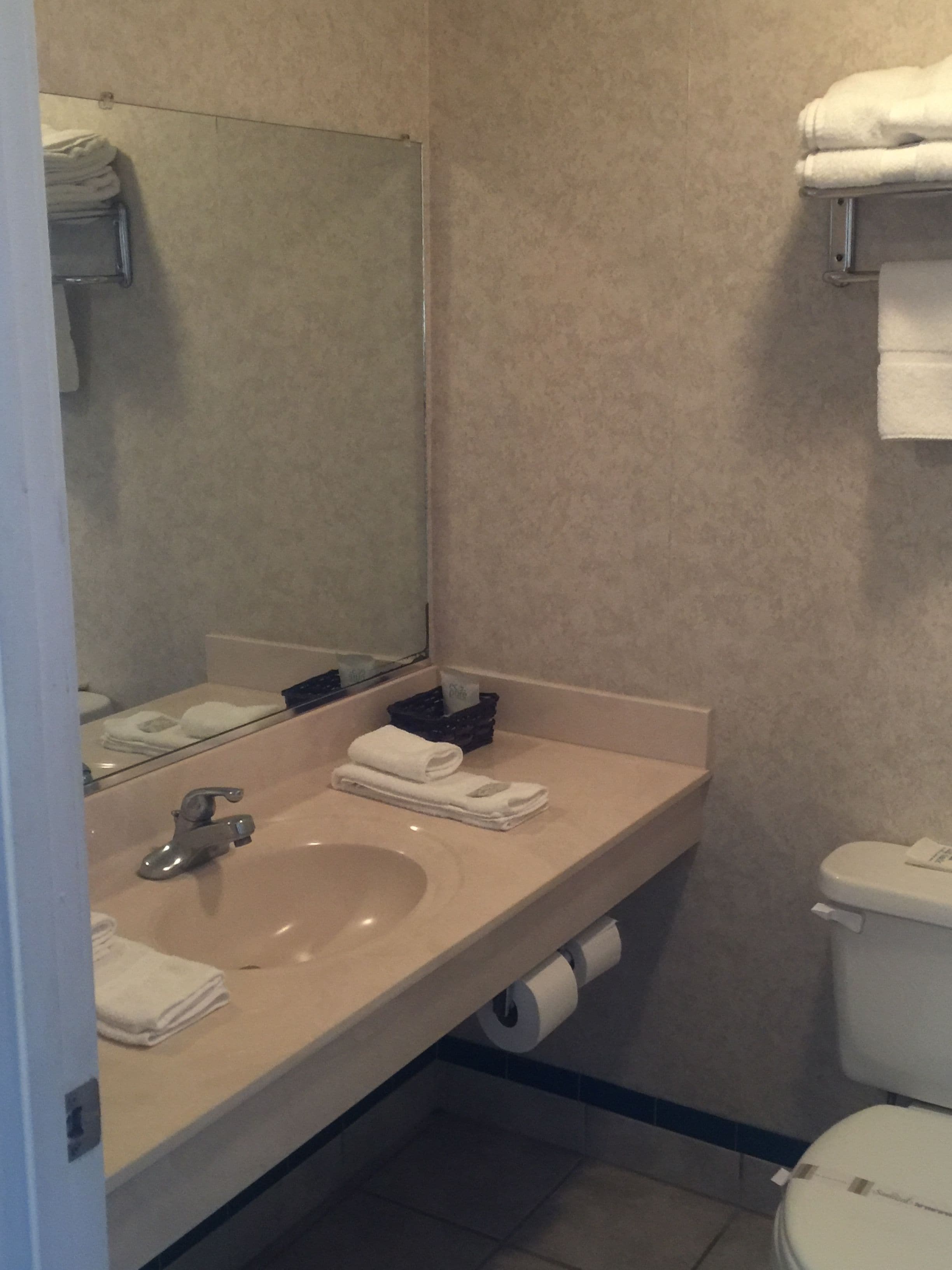 Een badkamer met een wastafel, spiegel en toilet. Handdoeken liggen gestapeld aan de muur en er is een rol toiletpapier op de vloer.