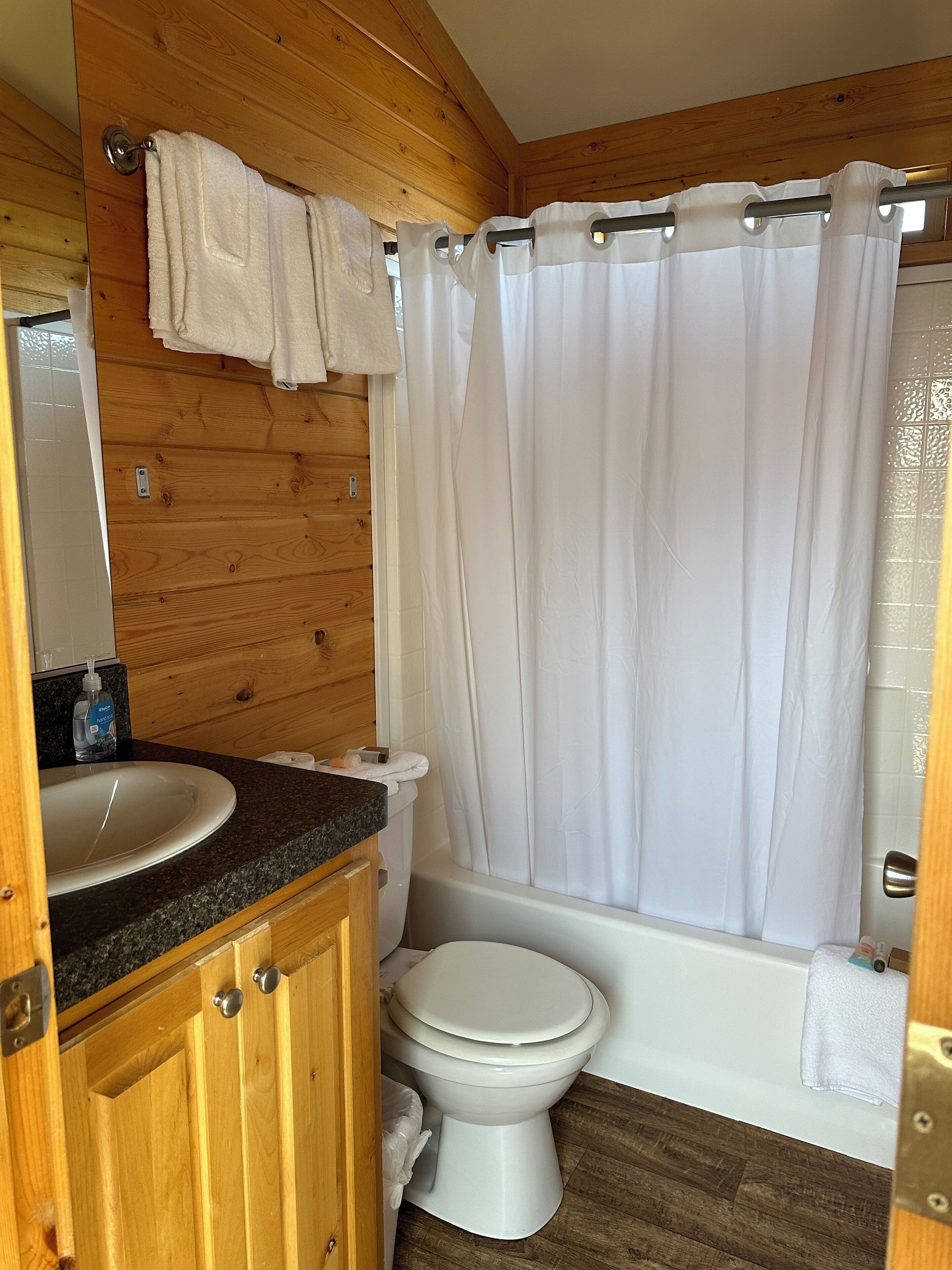 A wooden cabin bathroom with a sink, toilet, and shower curtain.