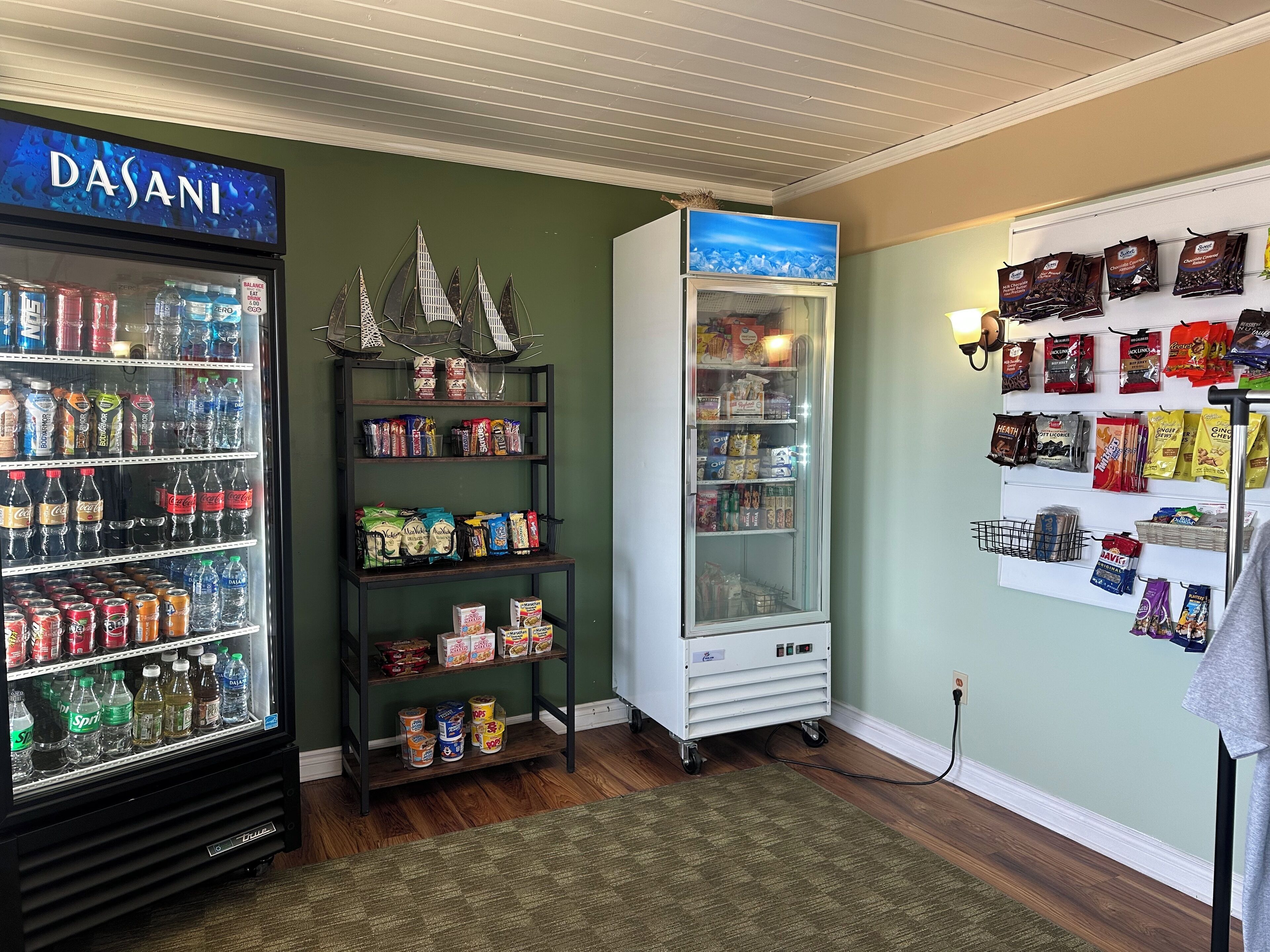 A vending machine stocked with snacks and beverages, a refrigerator with a 'DASANI' sign, and a wall displaying various packaged goods.