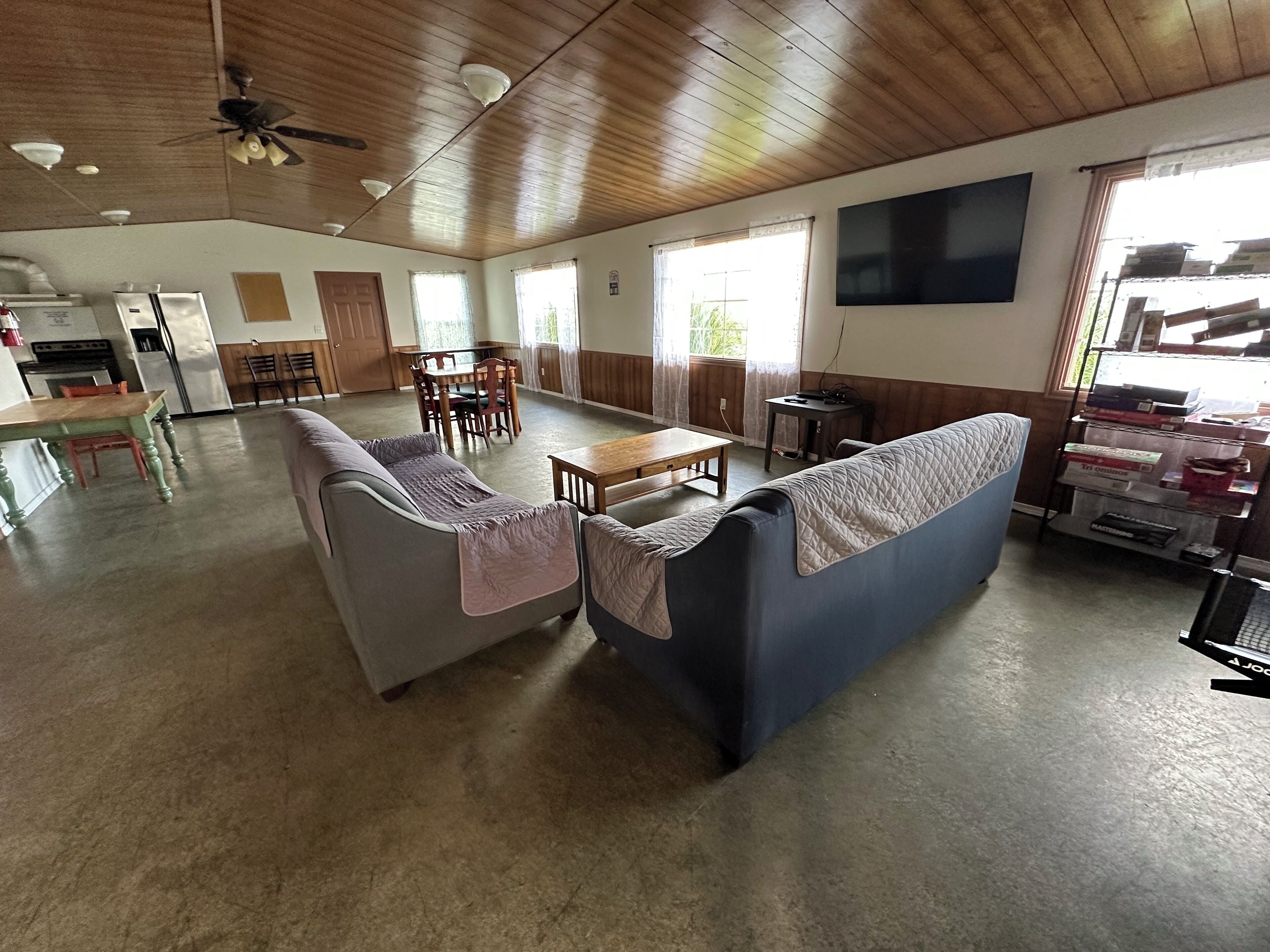 Amplia sala de estar con techo de madera, un sofá, una mesa de comedor y una cocina al fondo.