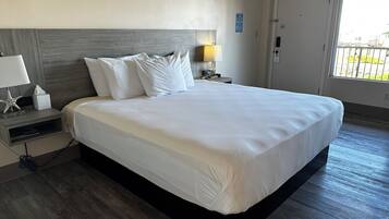 A hotel room with a large bed, a nightstand with a lamp, a starfish decoration, and a window with a view of the outside.