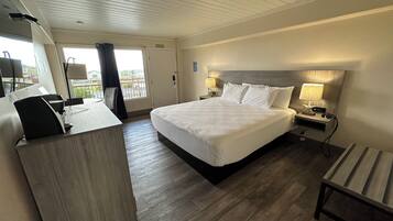 A hotel room with a large bed, a desk, a chair, and a view of the outside.
