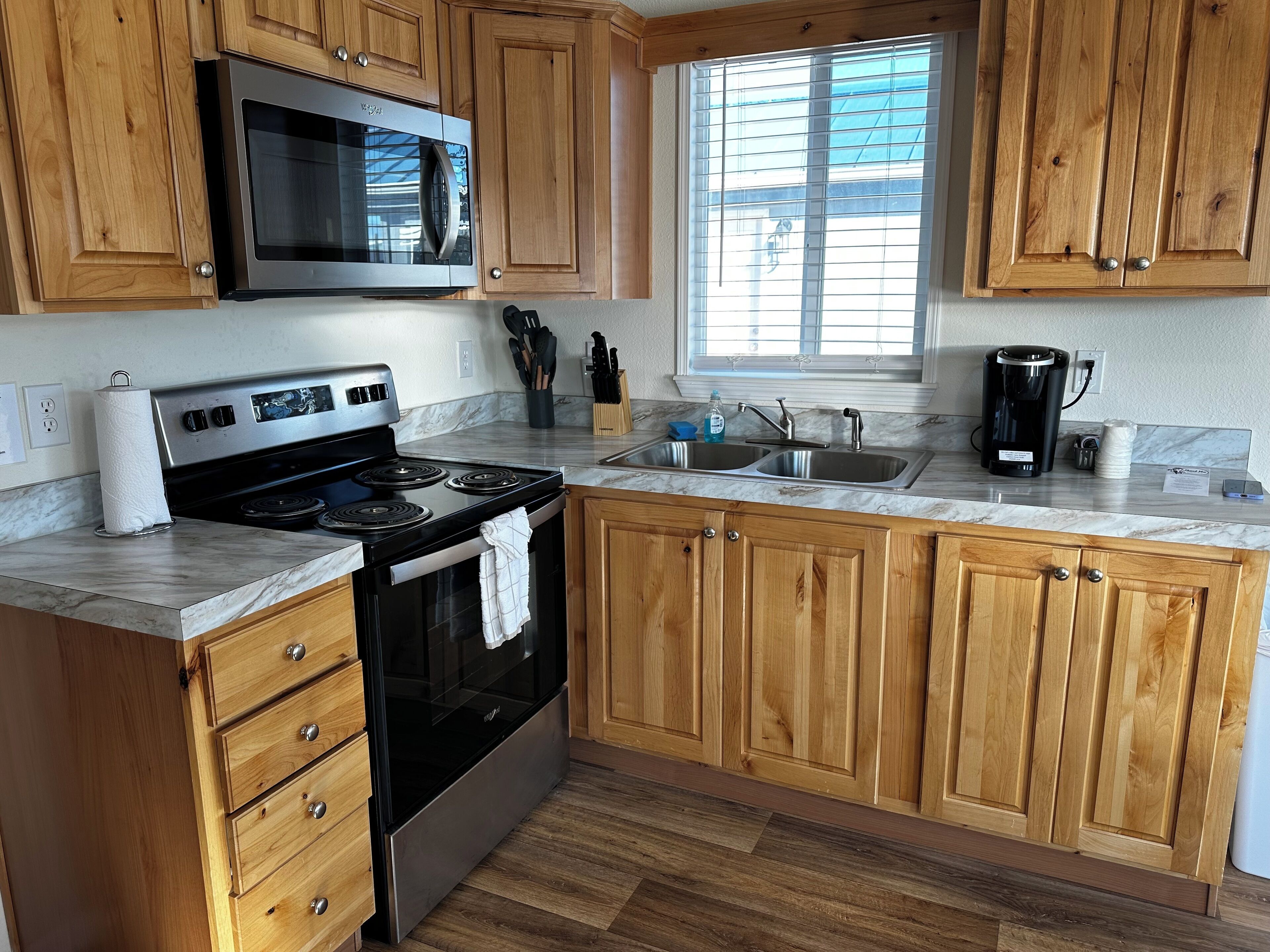 Una cocina con armarios de madera, una estufa de acero inoxidable, un microondas, un lavabo y una ventana con persianas.