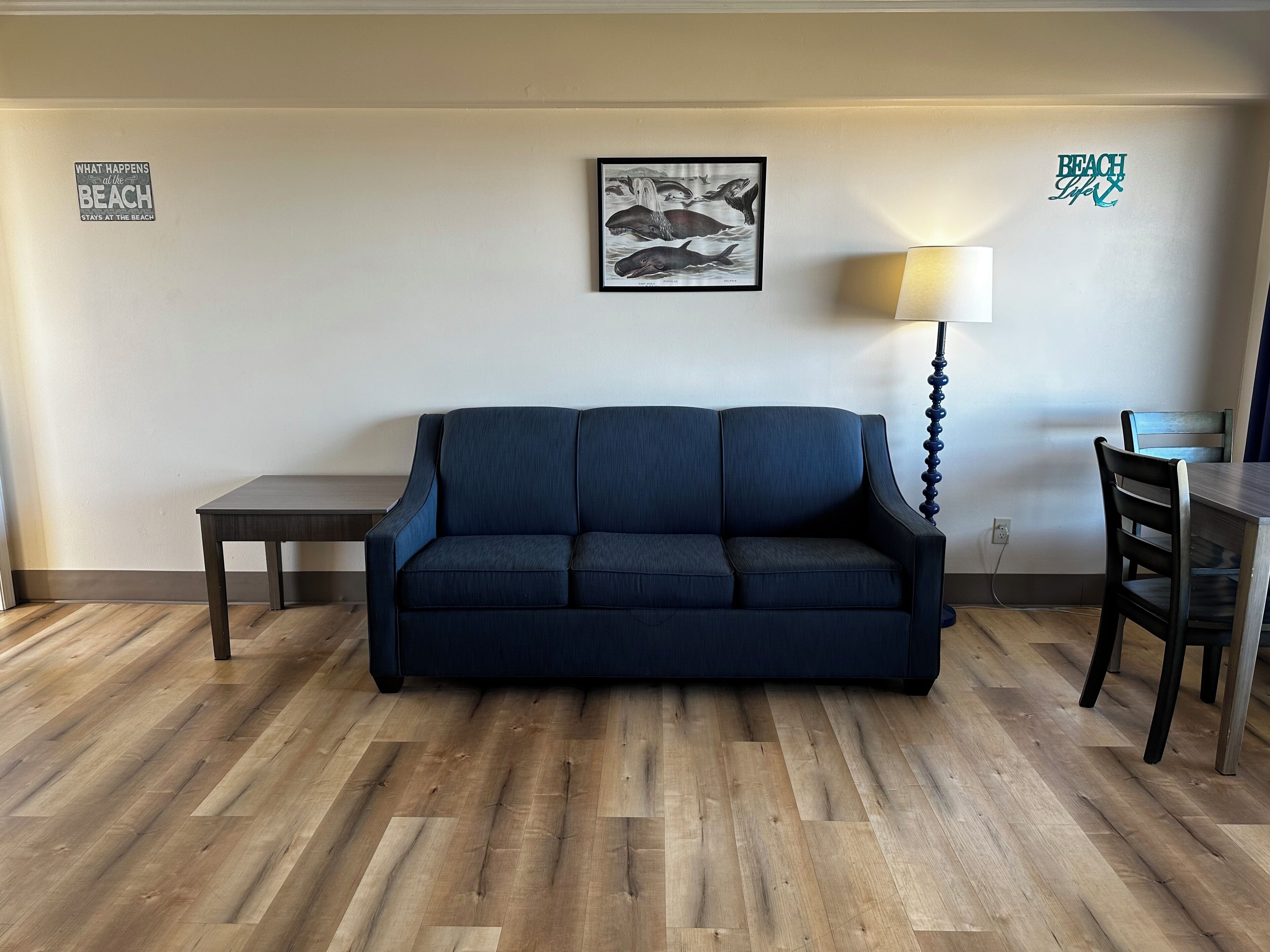 A room with a dark blue sofa, a small table, a lamp, and a framed illustration on the wall.