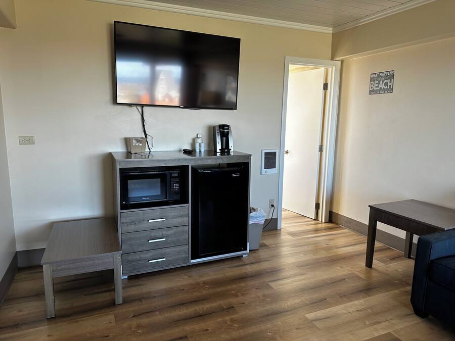 Una kitchenette compacta con microondas, cafetera y un televisor de pantalla plana montado arriba.