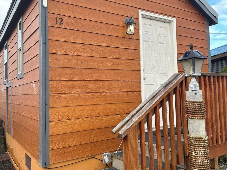 Eine Holzhütte mit weißer Tür, Hausnummer 12, und einer kleinen Veranda mit Holzgeländer.