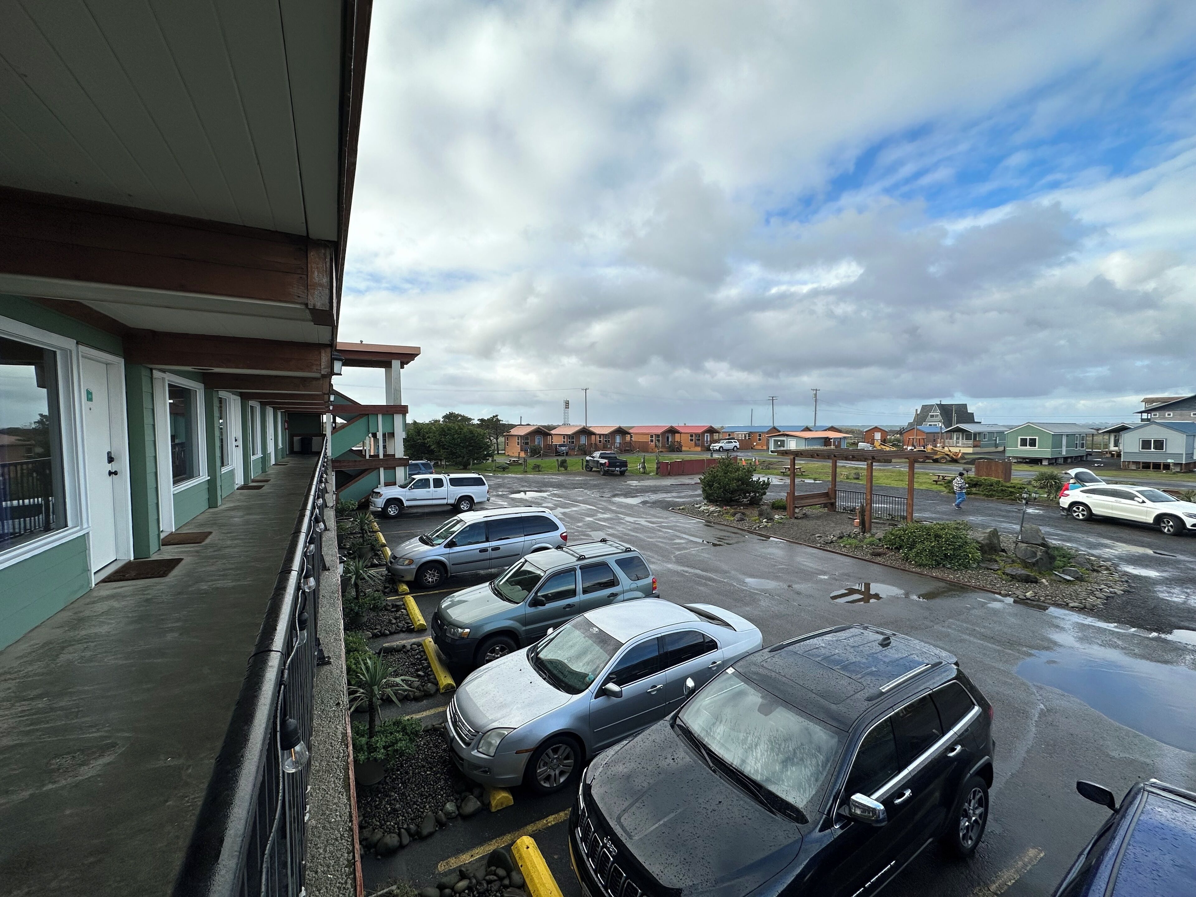 Een parkeerplaats met meerdere auto's, een gebouw met een groene gevel en een bewolkte lucht.