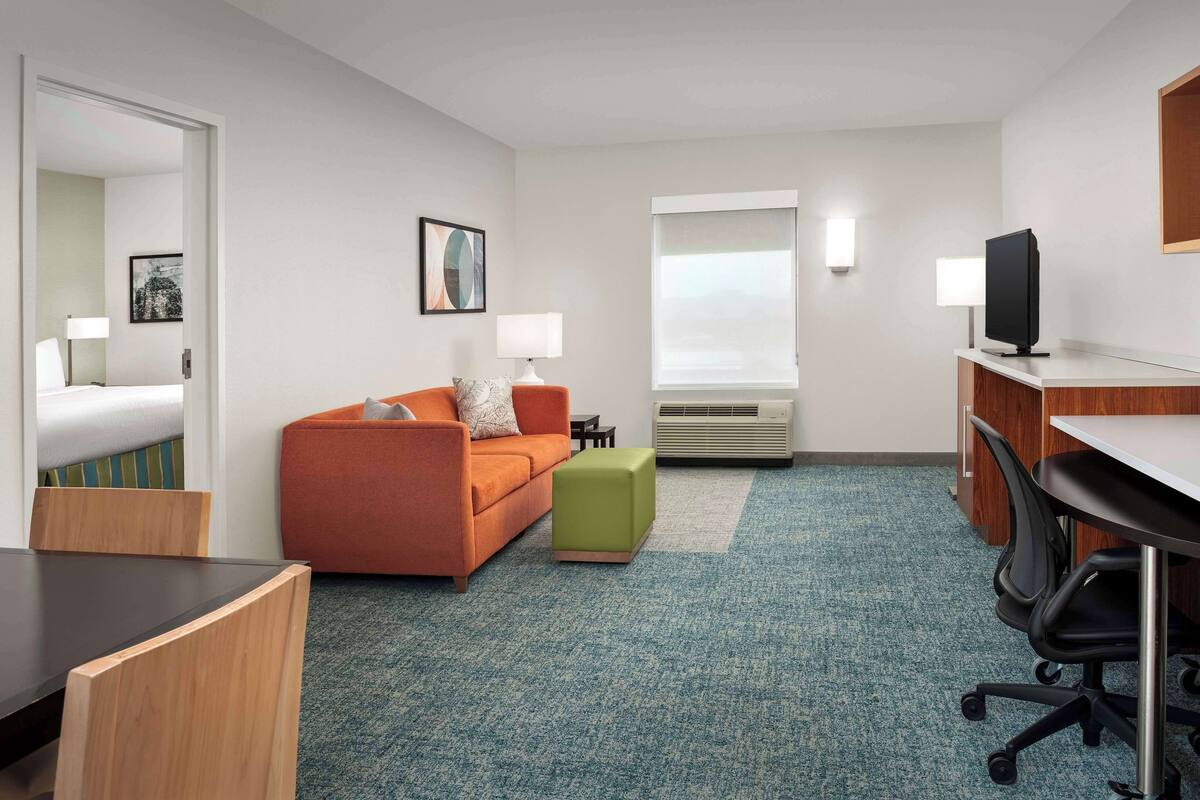 A hotel room with a bed, an orange sofa, a green ottoman, a desk with a computer, and a TV.