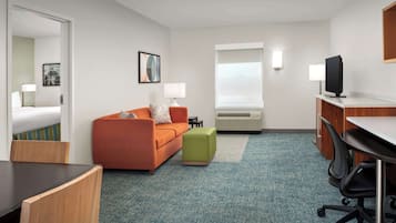 A hotel room with a bed, an orange sofa, a green ottoman, a desk with a computer, and a TV.