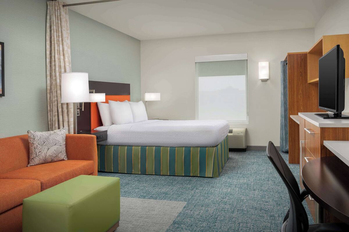 A hotel room with a bed, a sofa, a desk, and a television.