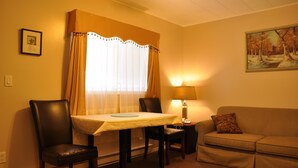 A room with a dining table, two chairs, a sofa, a lamp, and a painting on the wall. - Rosedale Motel (Summerland)