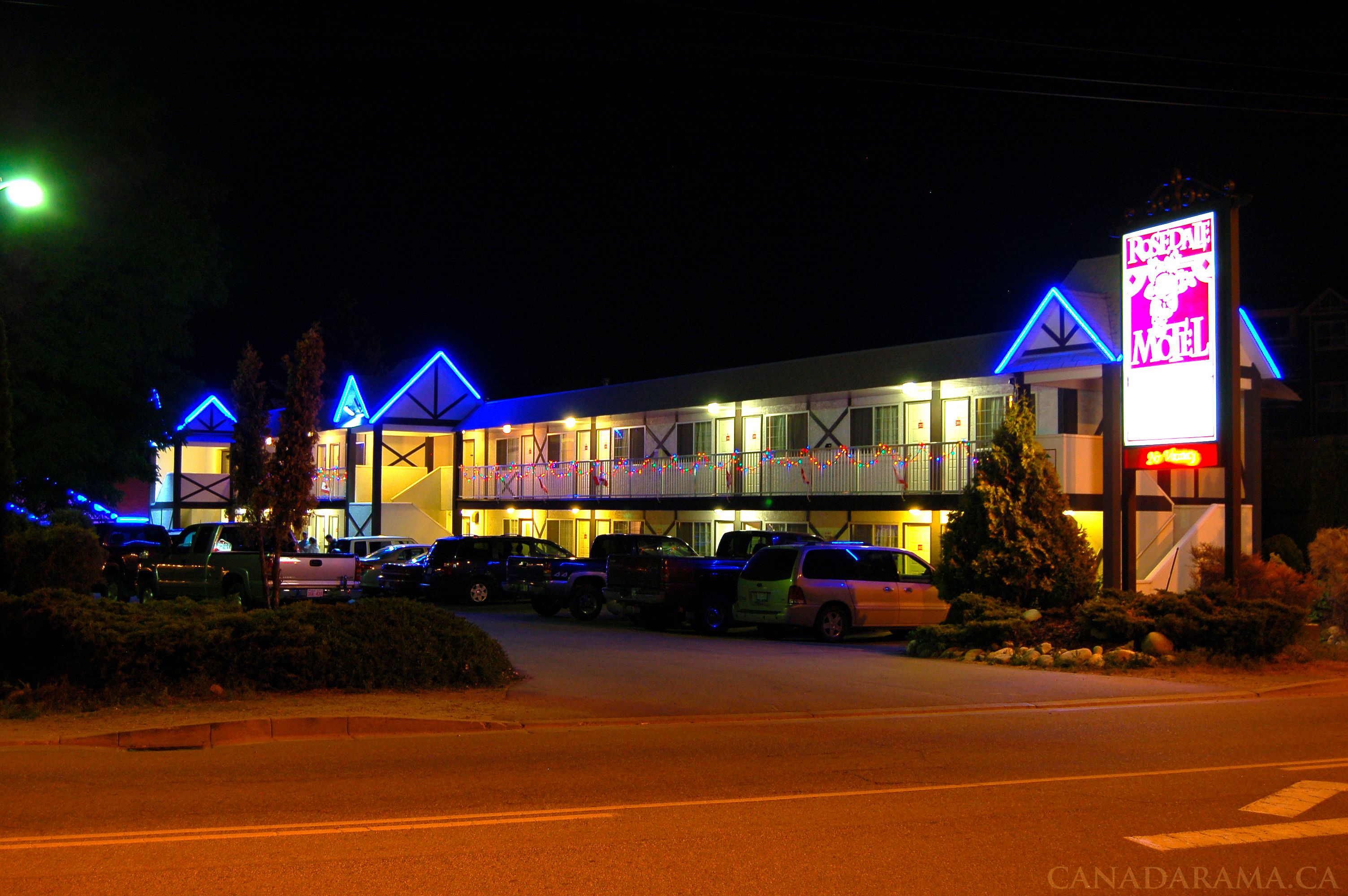 A motel with a two-story structure, a parking lot, and a neon sign advertising the motel.