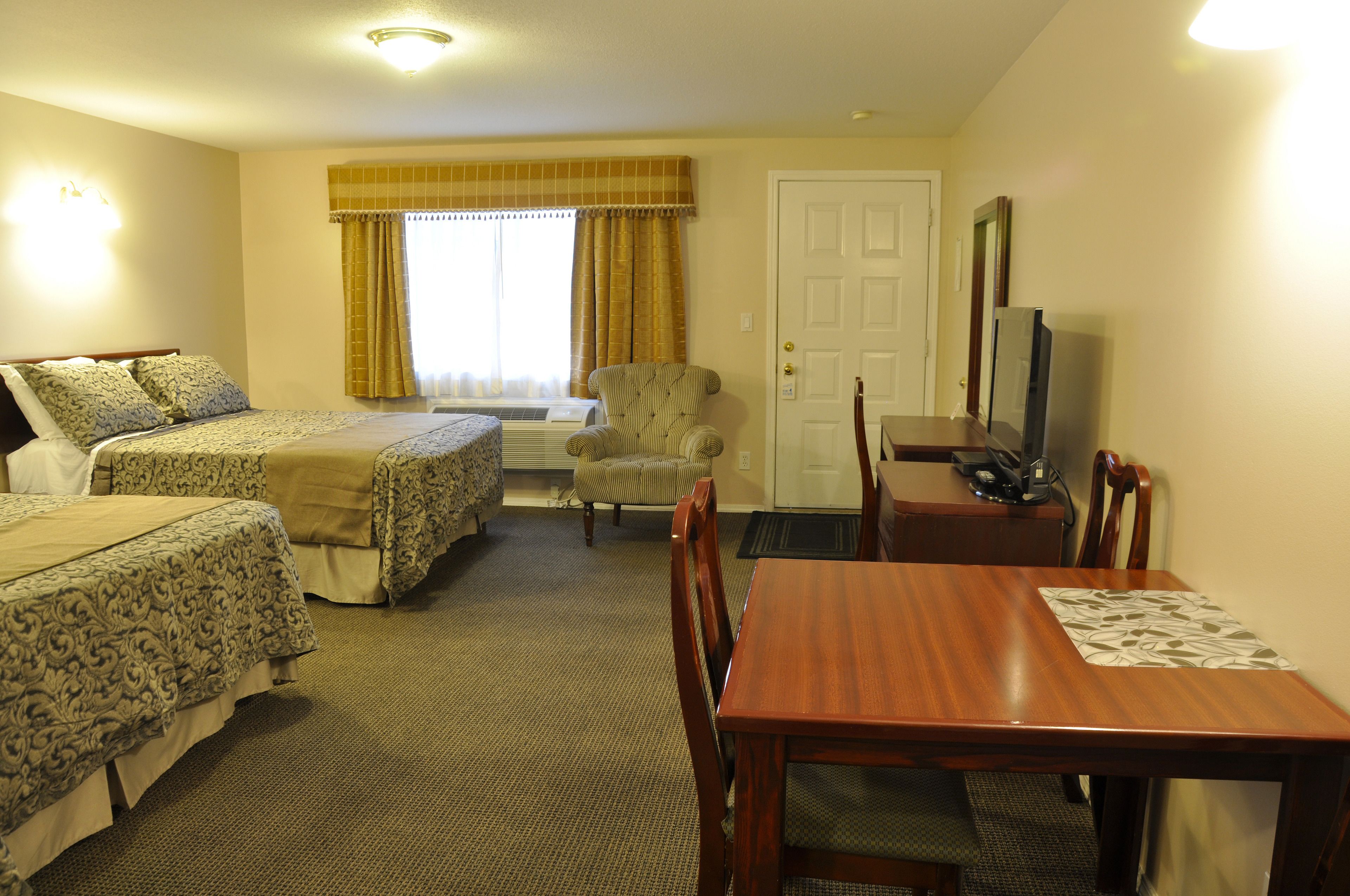 A hotel room with two beds, a dining table, a chair, a television, and a window with curtains.