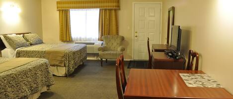 A hotel room with two beds, a dining table, a chair, a television, and a window with curtains.