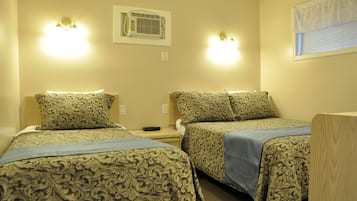 A hotel room with two beds, patterned bedding, wall-mounted lights, an air conditioning unit, and a window with blinds.