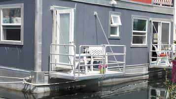 A houseboat with a covered deck, windows, and a small outdoor seating area.