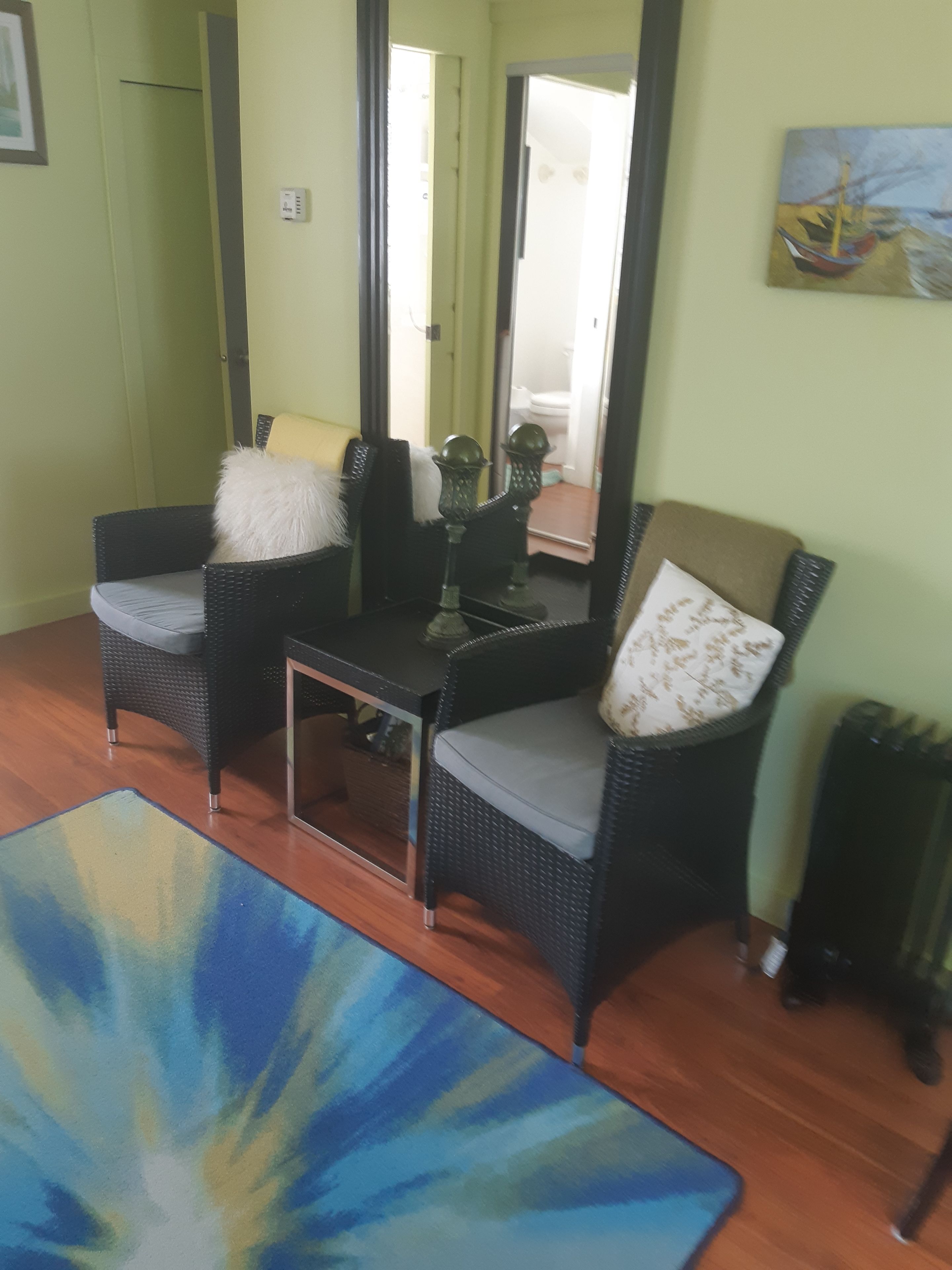 Ein Zimmer mit zwei Korbstühlen, einem kleinen Tisch, einem Spiegel und einem blauen Teppich.