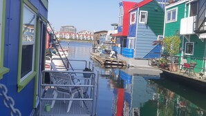 A narrow waterway with colorful buildings on either side, a dock with a swing chair, and a clear sky. - A Float Home B&B in Fisherman’s Wharf (Victoria)