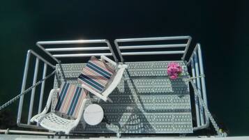 A deck with two striped lounge chairs and a small table, surrounded by metal railings.