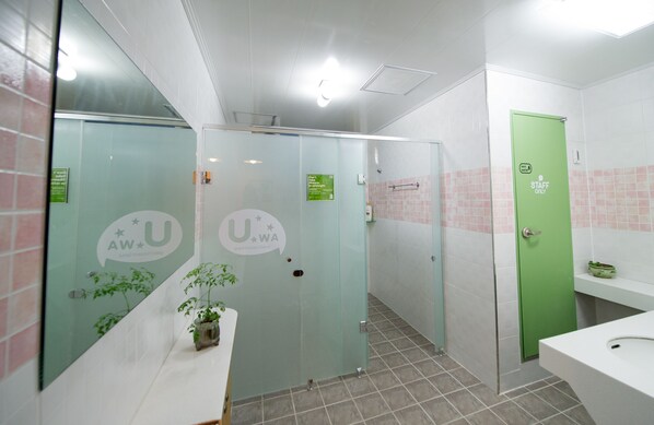 Des toilettes avec des cloisons en verre, une porte verte réservée au personnel et un lavabo blanc.