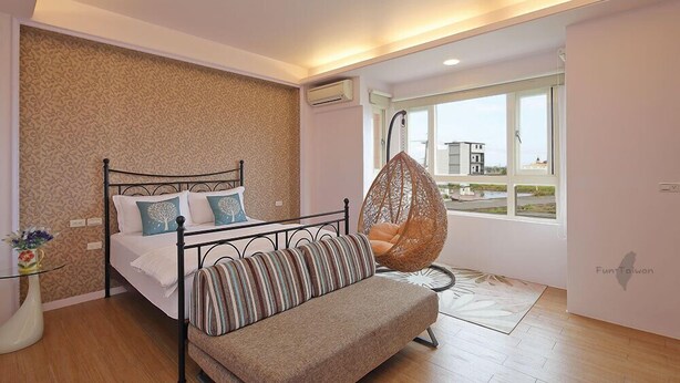 A bedroom with a bed, a hanging chair, a sofa, a vase with flowers, and a window with a view.