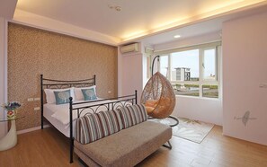 Un dormitorio con cama, una silla colgante, un sofá, un jarrón con flores y una ventana con vistas.