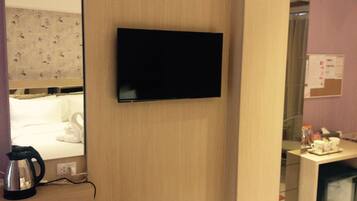 Habitación de hotel con televisión de pantalla plana montada en una pared de madera, tetera en la encimera y cama con ropa blanca.