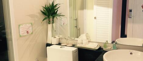 A bathroom with a toilet, sink, and shower. There is a sign on the wall and a plant on the counter.