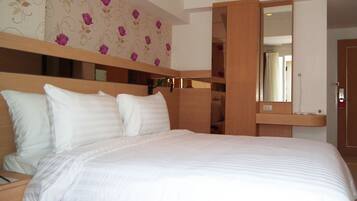 A hotel room with a large bed, a wooden headboard, a wardrobe, and a mirror.