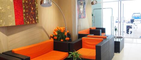 Un área de recepción con asientos naranja, un jarrón con flores y una revista sobre una mesa.