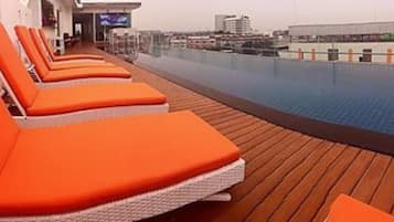 Área de piscina com cadeiras de descanso laranja e um deck de madeira.
