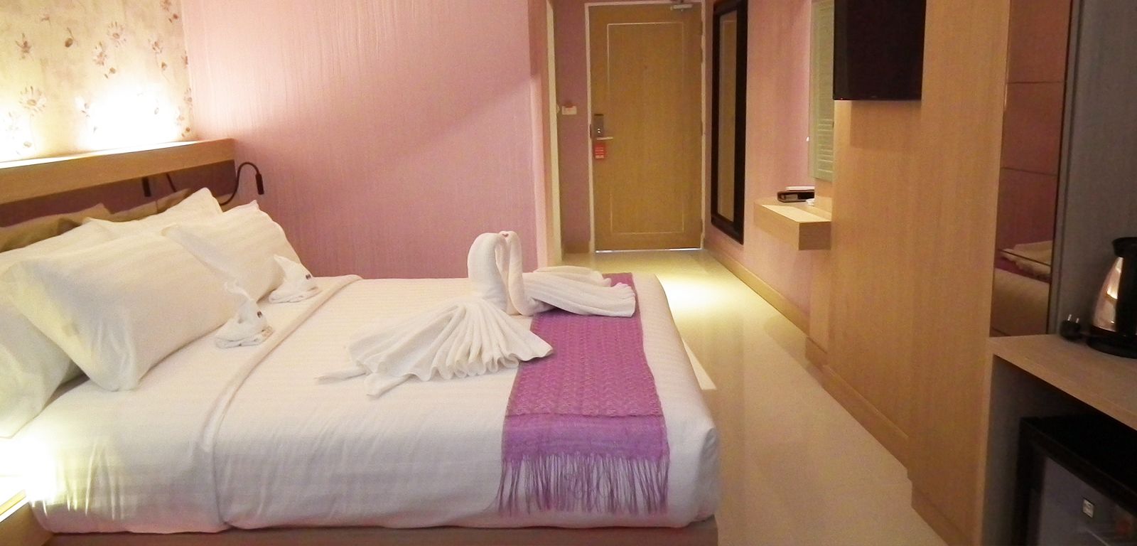 A hotel room with a neatly made bed, a bedside table with a lamp, and a door leading to another room.