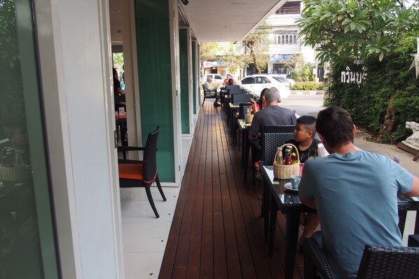 An outdoor seating area with tables and chairs, a wooden deck, and a view of the street. - Kavin Buri Green Hotel (Udon Thani)