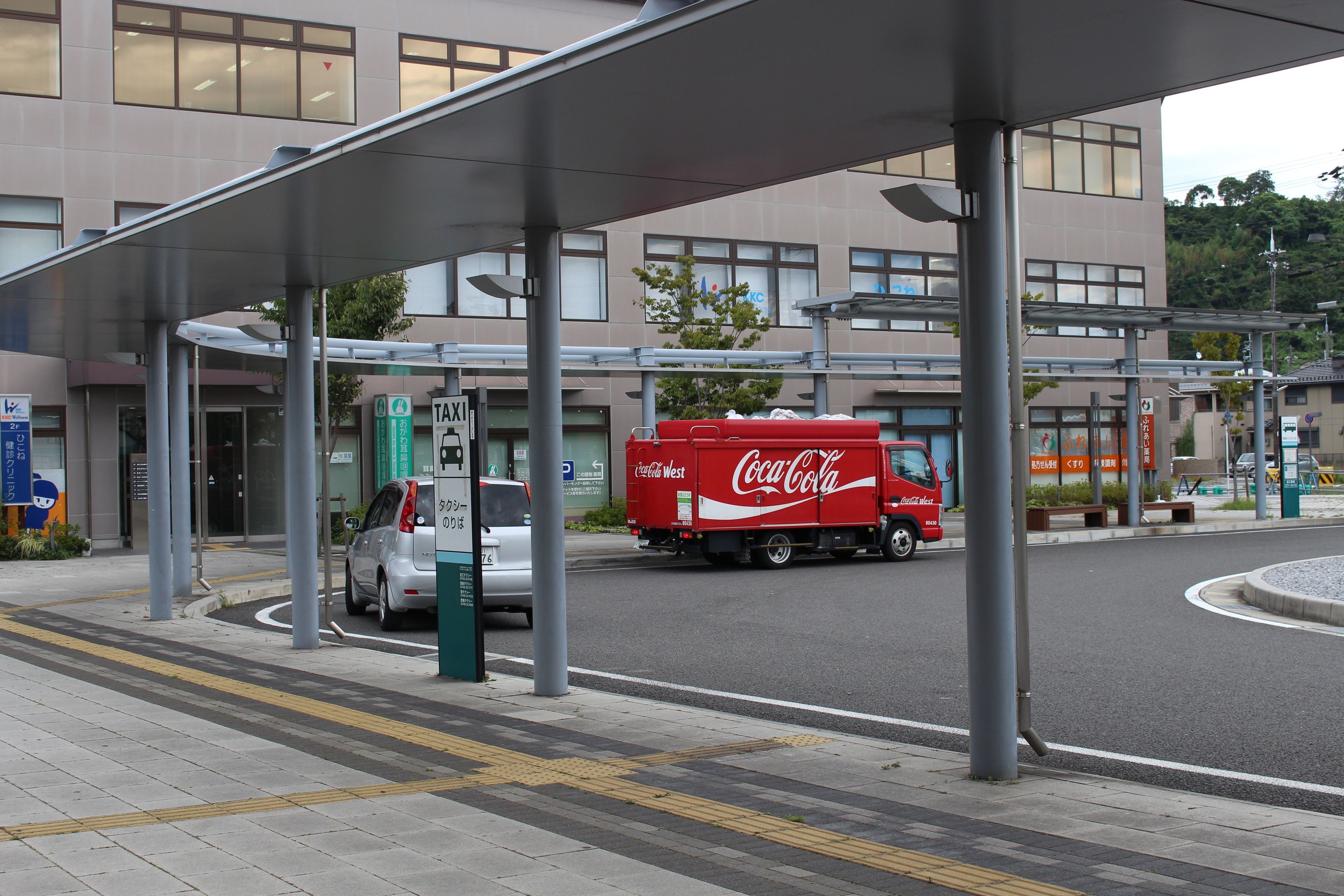 Un edificio moderno con un acceso cubierto, un camión de Coca-Cola y una zona de estacionamiento.