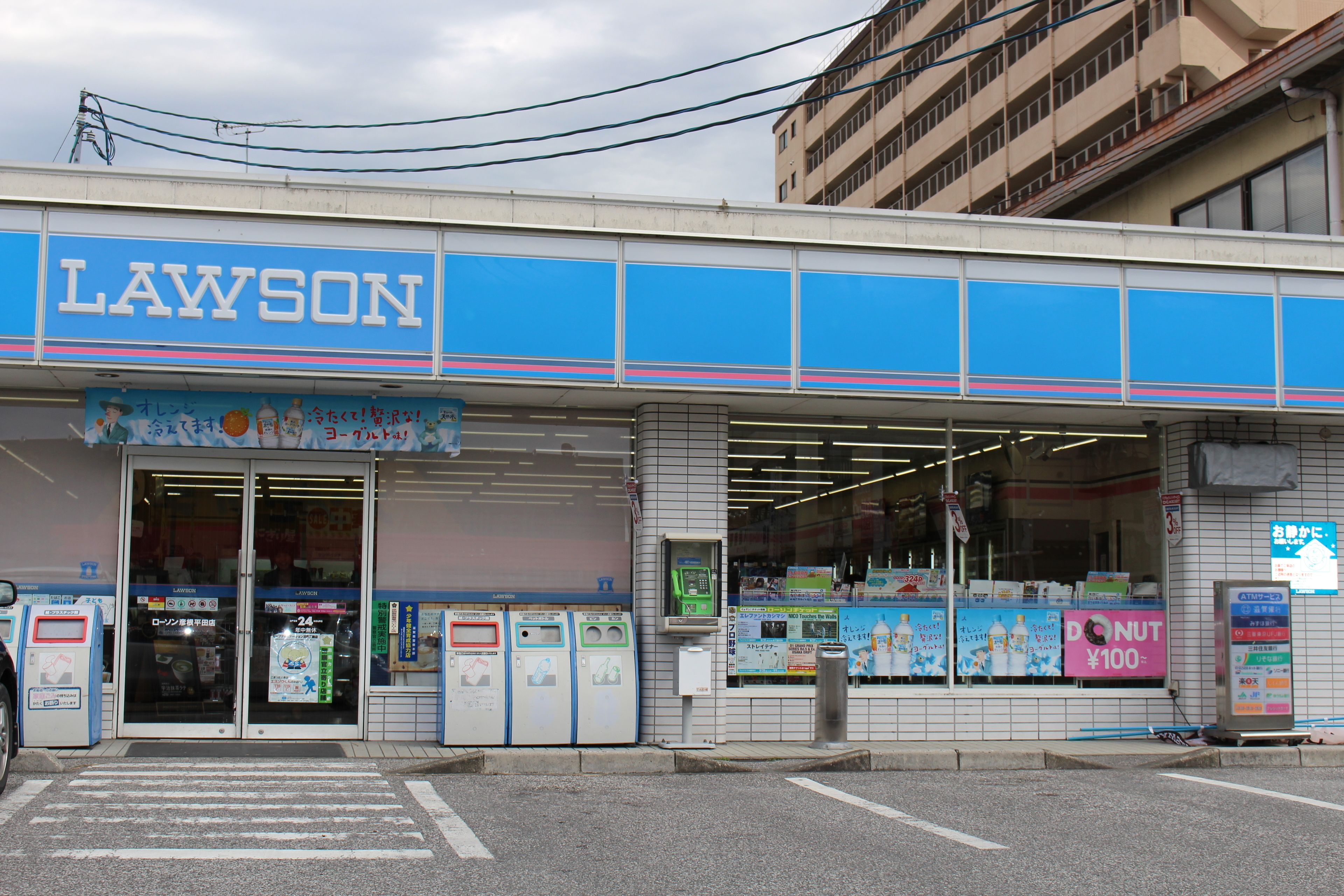 A Lawson convenience store with a blue and white facade, entrance, and visible vending machines.
