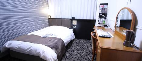 A hotel room with a bed, a desk, a chair, a mirror, and a window with curtains.
