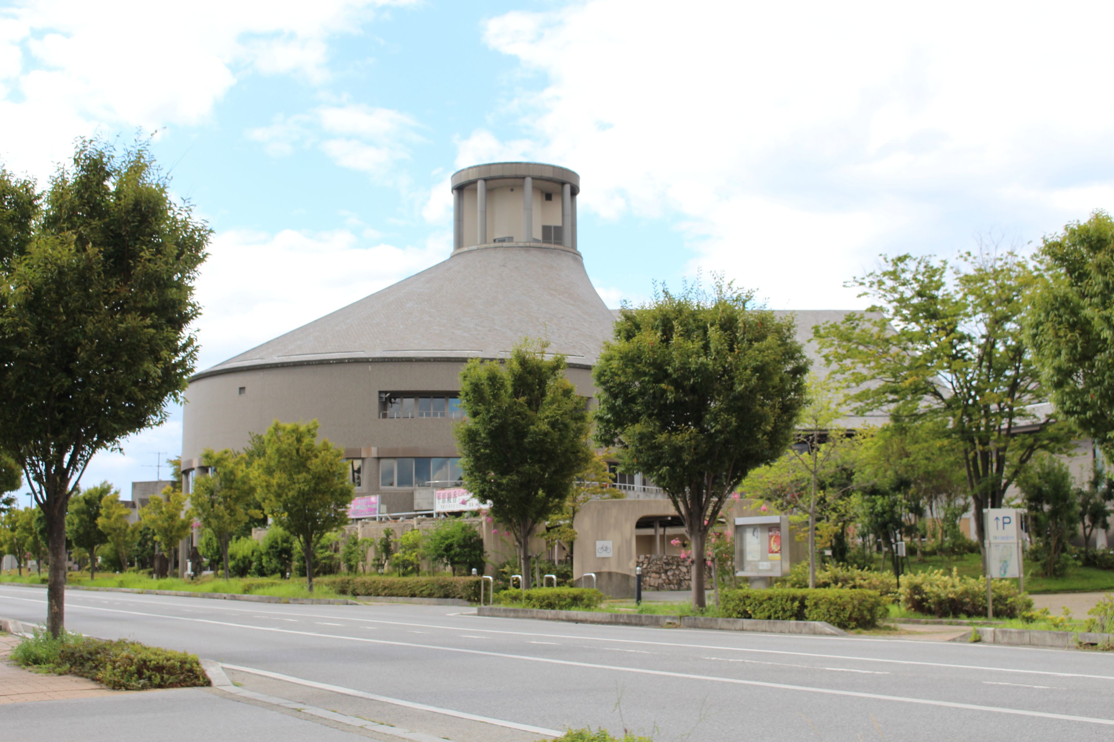 A modern building with a unique dome structure, surrounded by trees and a clear sky.