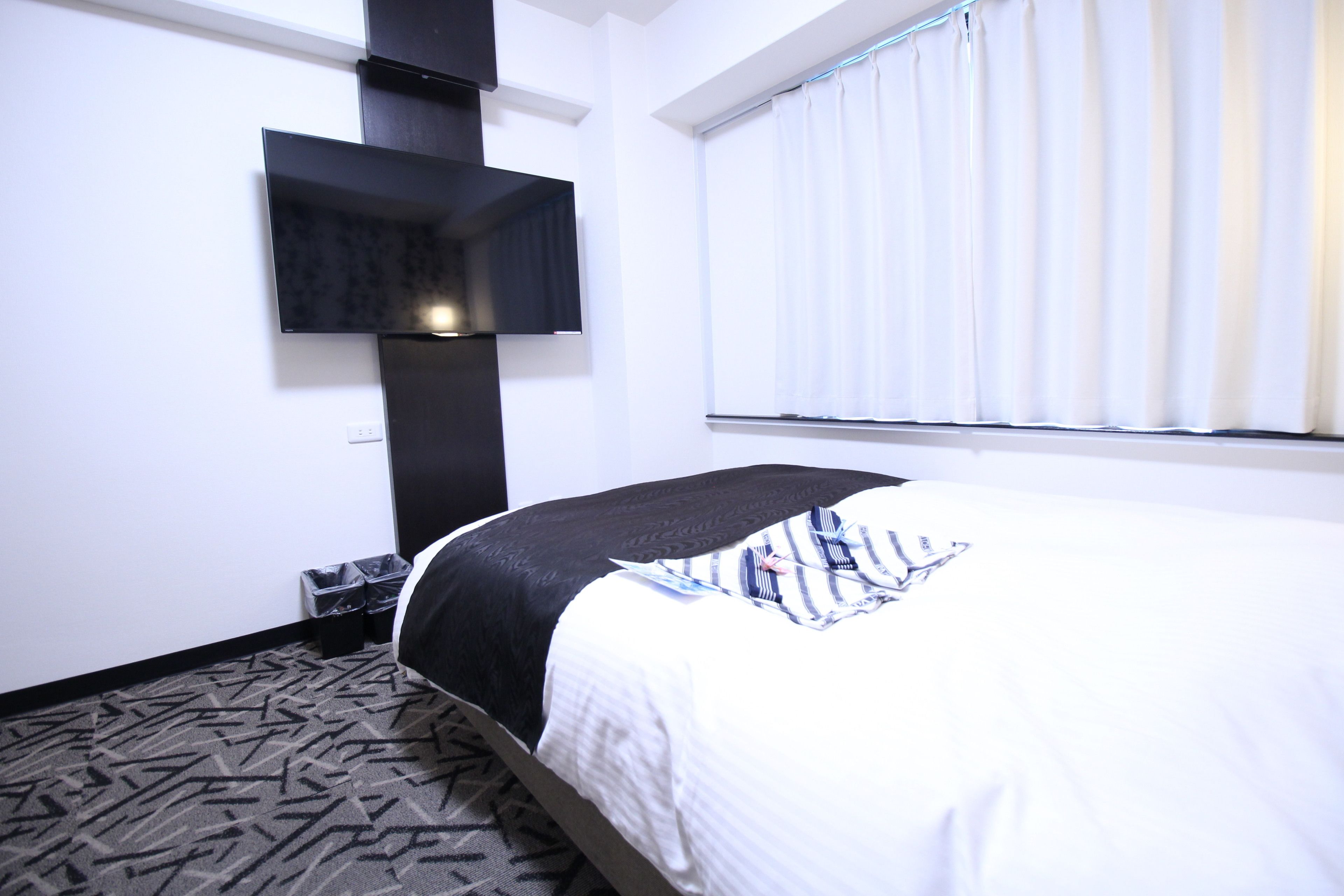 Una camera d'albergo con un letto, una TV a schermo piatto montata a parete, una finestra con persiane e un tappeto decorato.