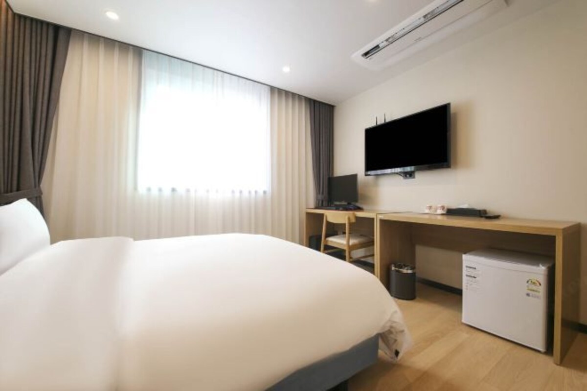 A hotel room with a large bed, a desk with a computer, a television, and a mini-fridge.
