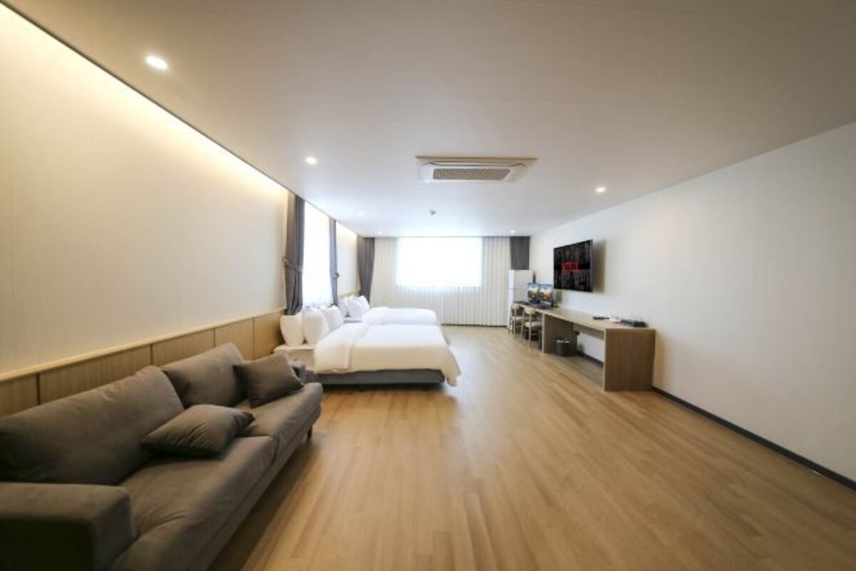 A modern hotel room with a large bed, a sofa, a desk, and a TV.