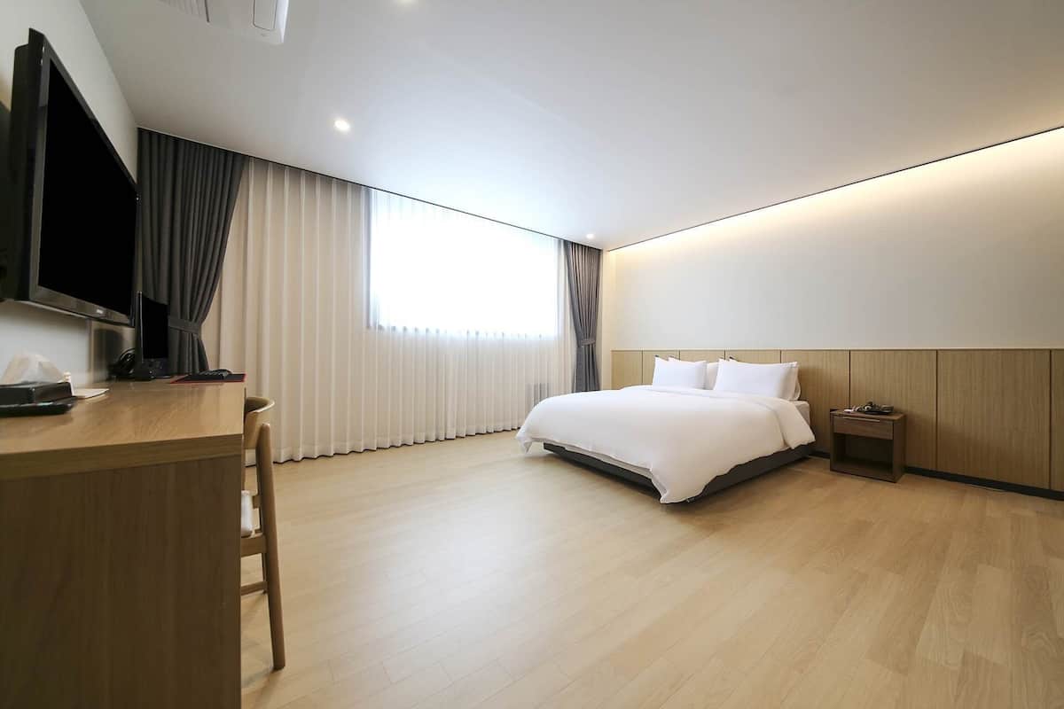 A modern hotel room with a large bed, a desk with a chair, a TV, and a bedside table.
