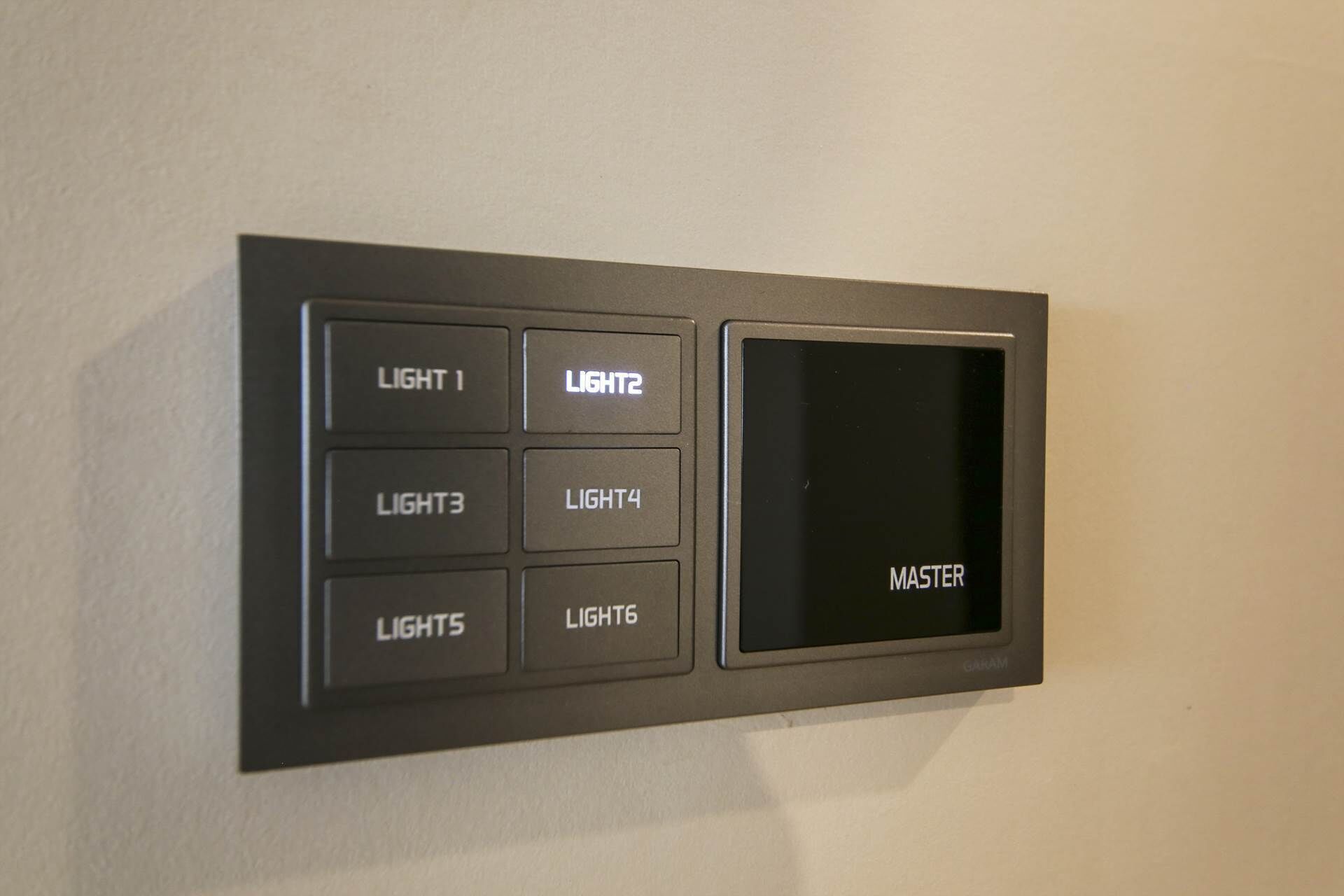 Painel de controlo fixado na parede com botões identificados para LUZ 1, LUZ 2, LUZ 3, LUZ 4, LUZES, LUZ 6 e um interruptor MESTRE.