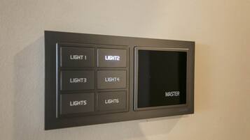 Painel de controlo fixado na parede com botões identificados para LUZ 1, LUZ 2, LUZ 3, LUZ 4, LUZES, LUZ 6 e um interruptor MESTRE.