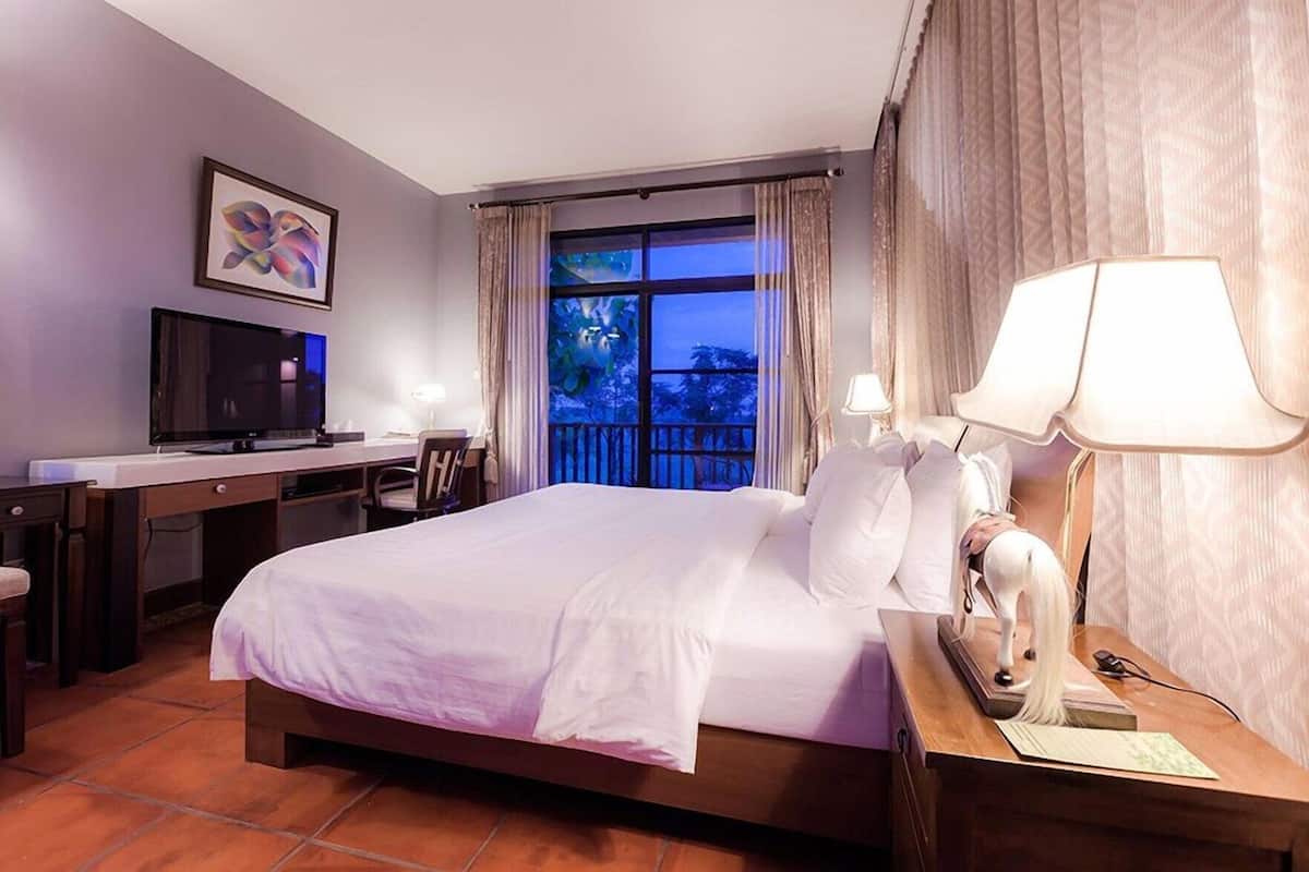 A hotel room with a bed, desk, TV, and a balcony view.