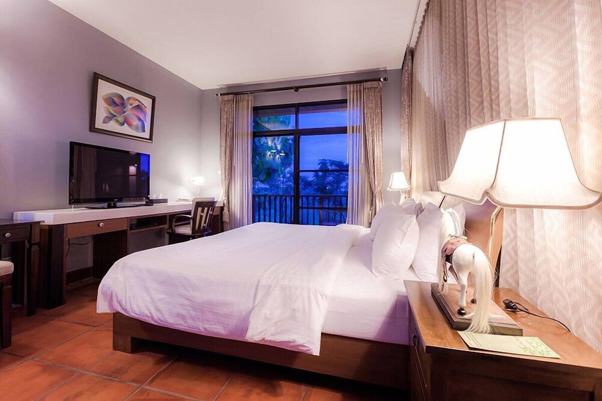 Quarto de hotel com cama, escrivaninha, televisão e vista para a varanda.